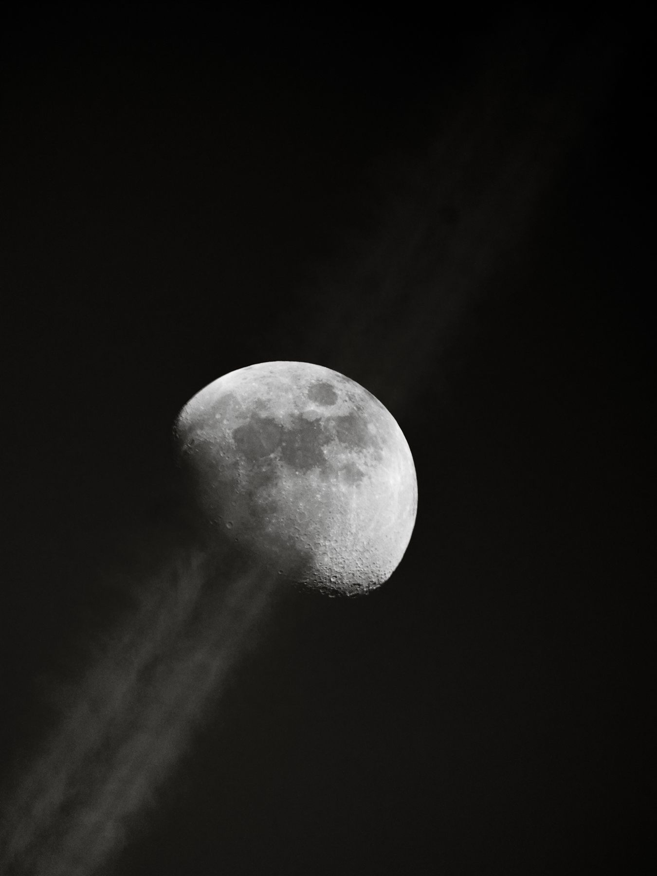 Lune gibbeuse traversée par une traînée de condensation, noir et blanc