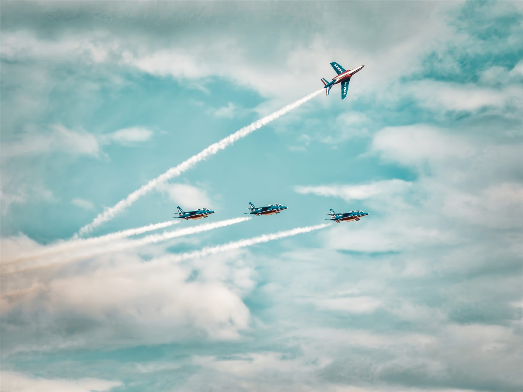 Quatre avions de la Patrouille de France, l'un s'échappant vers le ciel