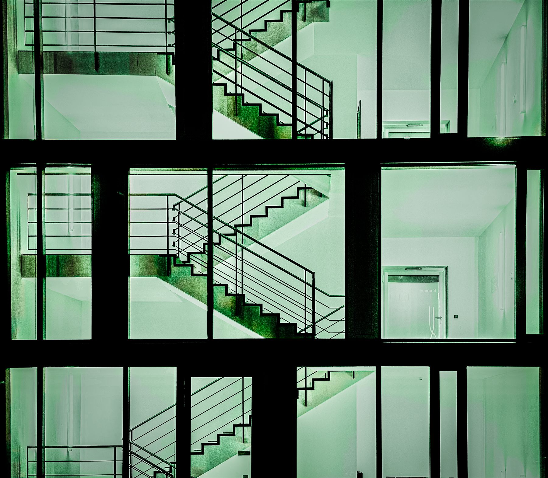 Cages d'escalier vues de nuit à travers une façade vitrée, lumière verte